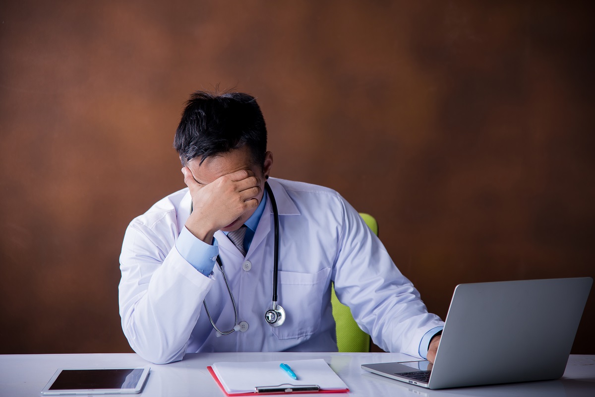 doctor resting his head on one hand while using a laptop with the other