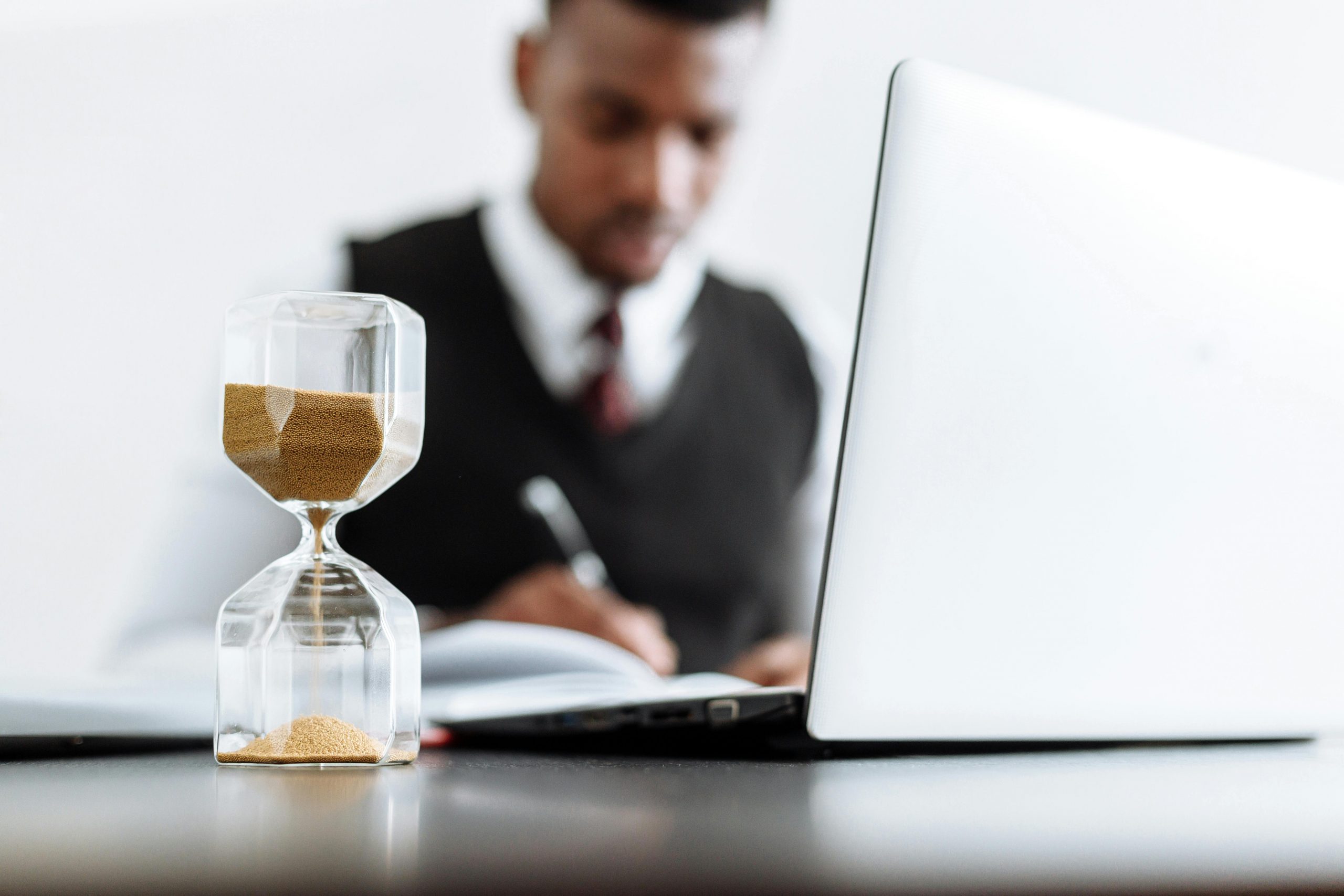 a laptop and an hourglass on a desk with a lawyer working in the background