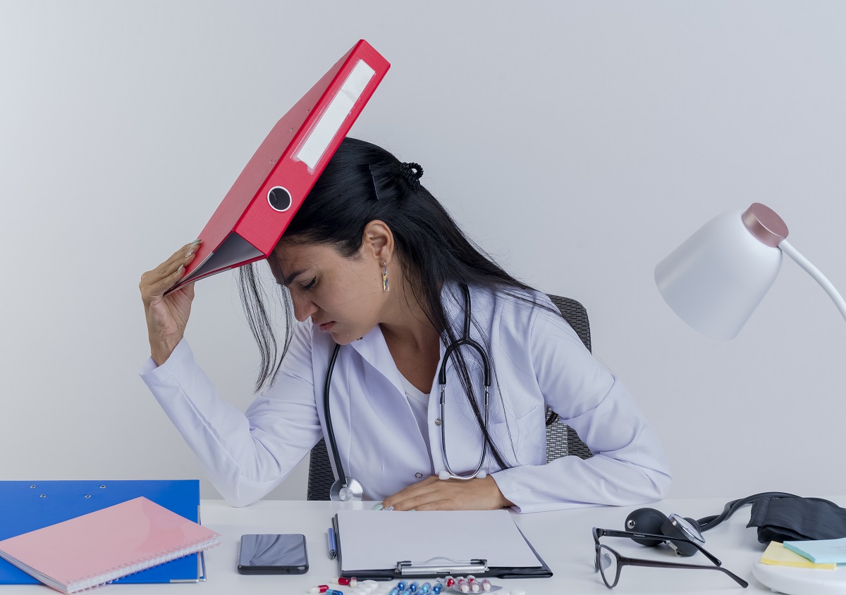 frustrated female doctor tapping her forehead with a binder